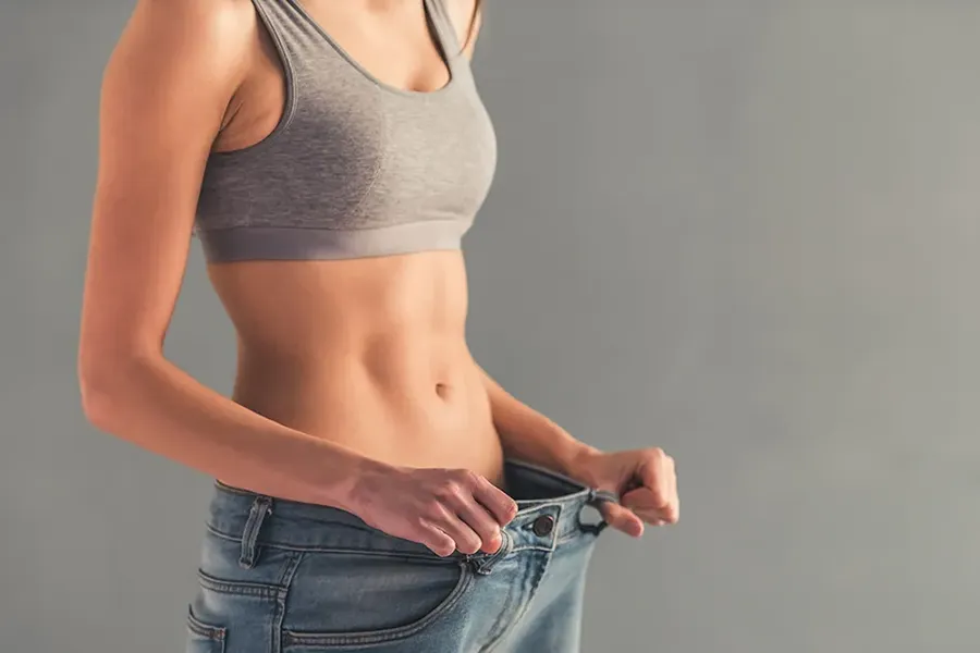 Abdominal-Weight-Loss-Clinic A woman who has lost weight holds her jeans away from her waist. Schedule abdominal weight loss treatment from Healthy Aging Medical Centers of New Jersey in Northern New Jersey.