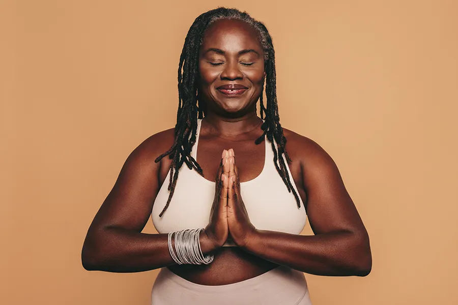 Obesity-Clinic An older African American woman confidently posing against a warm background smiling with hands in a prayer pose. Healthy Aging Medical Centers of New Jersey treats obesity using functional medicine in Northern New Jersey.