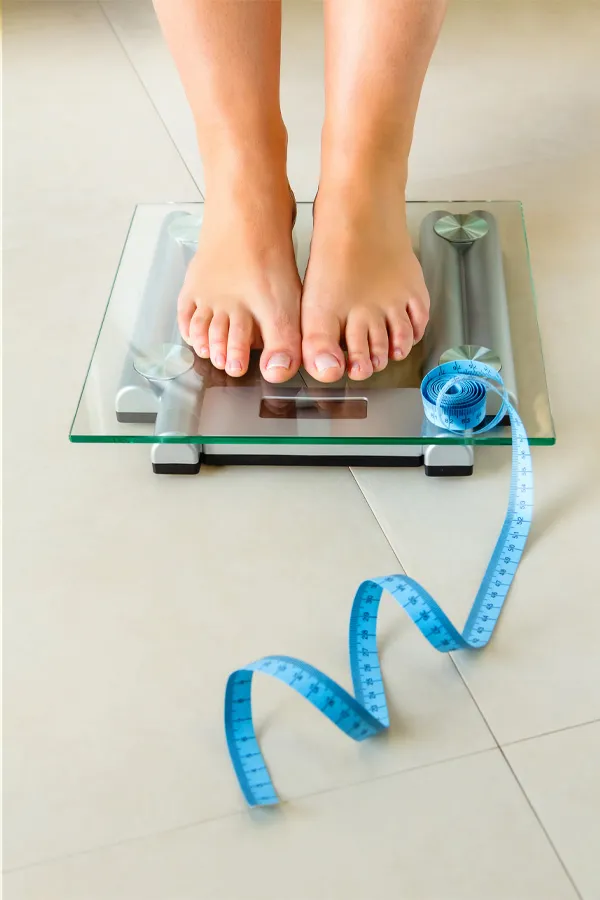 Post-Surgical-Weight-Loss-Treatment A woman stands on a scale. Get post-surgical weight loss treatment from Healthy Aging Medical Centers of New Jersey in Northern New Jersey.