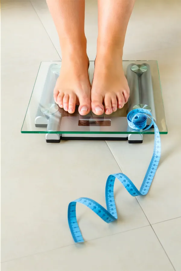 Weight-Loss-Resistance-Treatment Close-up of a woman's feet standing on a scale, with measuring tape by her toes, getting treatment for weight loss resistance from Healthy Aging Medical Centers of New Jersey in Northern New Jersey.
